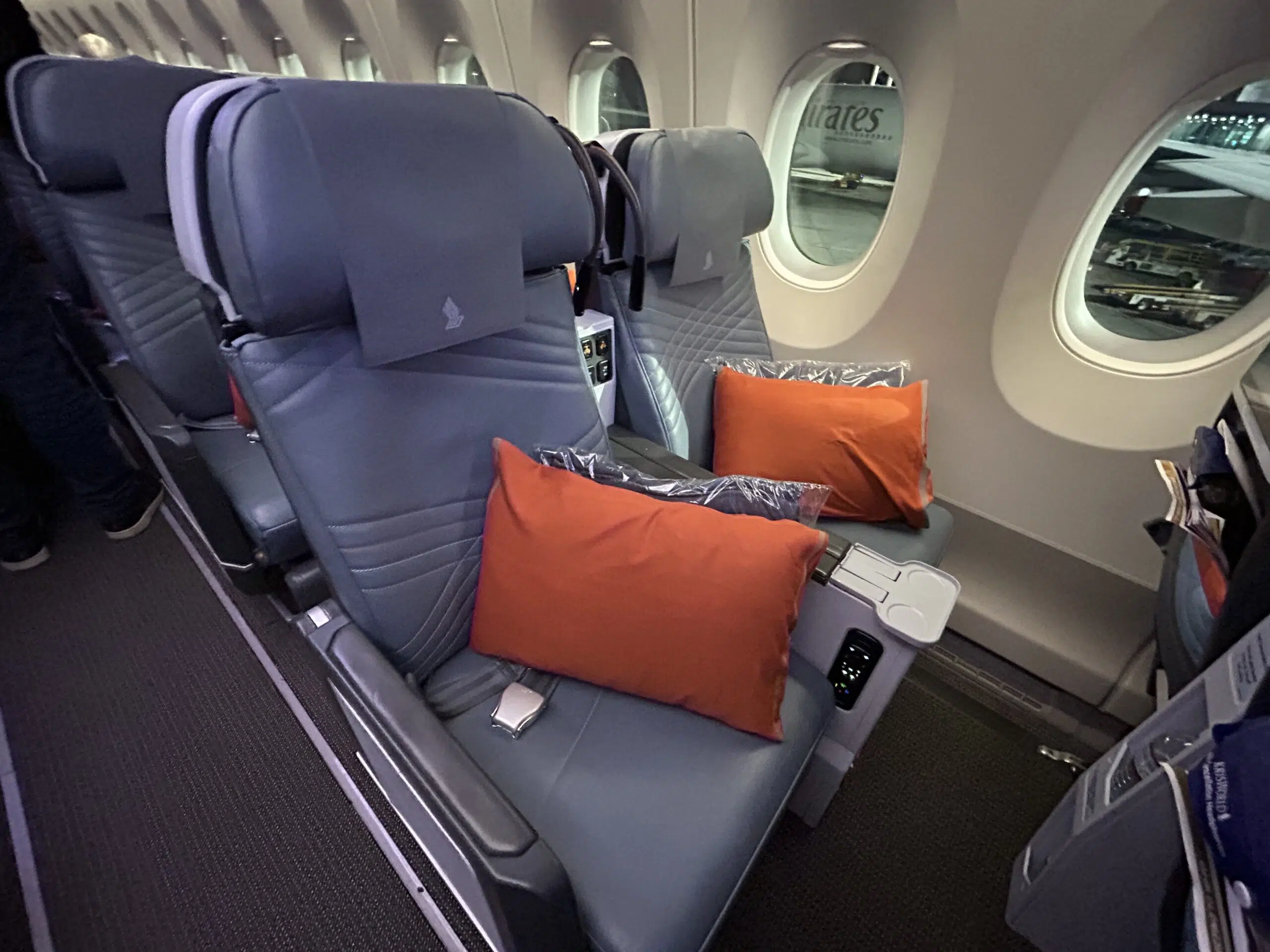 two empty window seats on an airplane with two orange pillows 