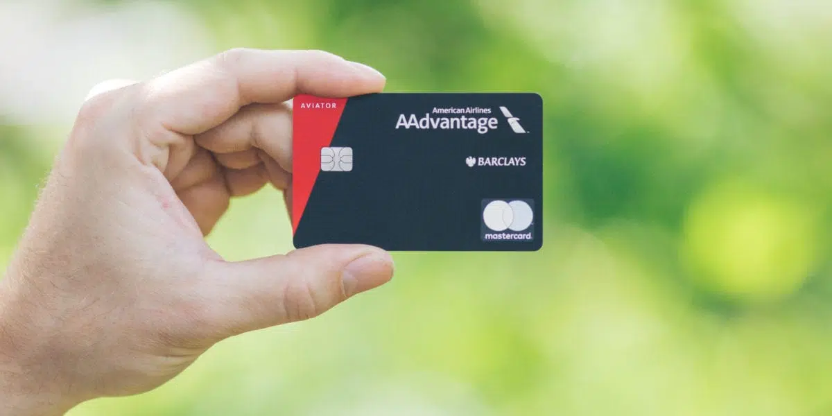 A hand holding the Aviator Red Mastercard with a green background.