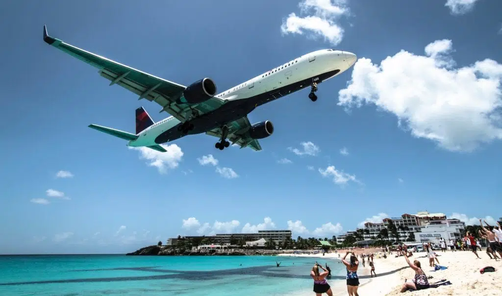 A Delta airplane flying over a crowded beach