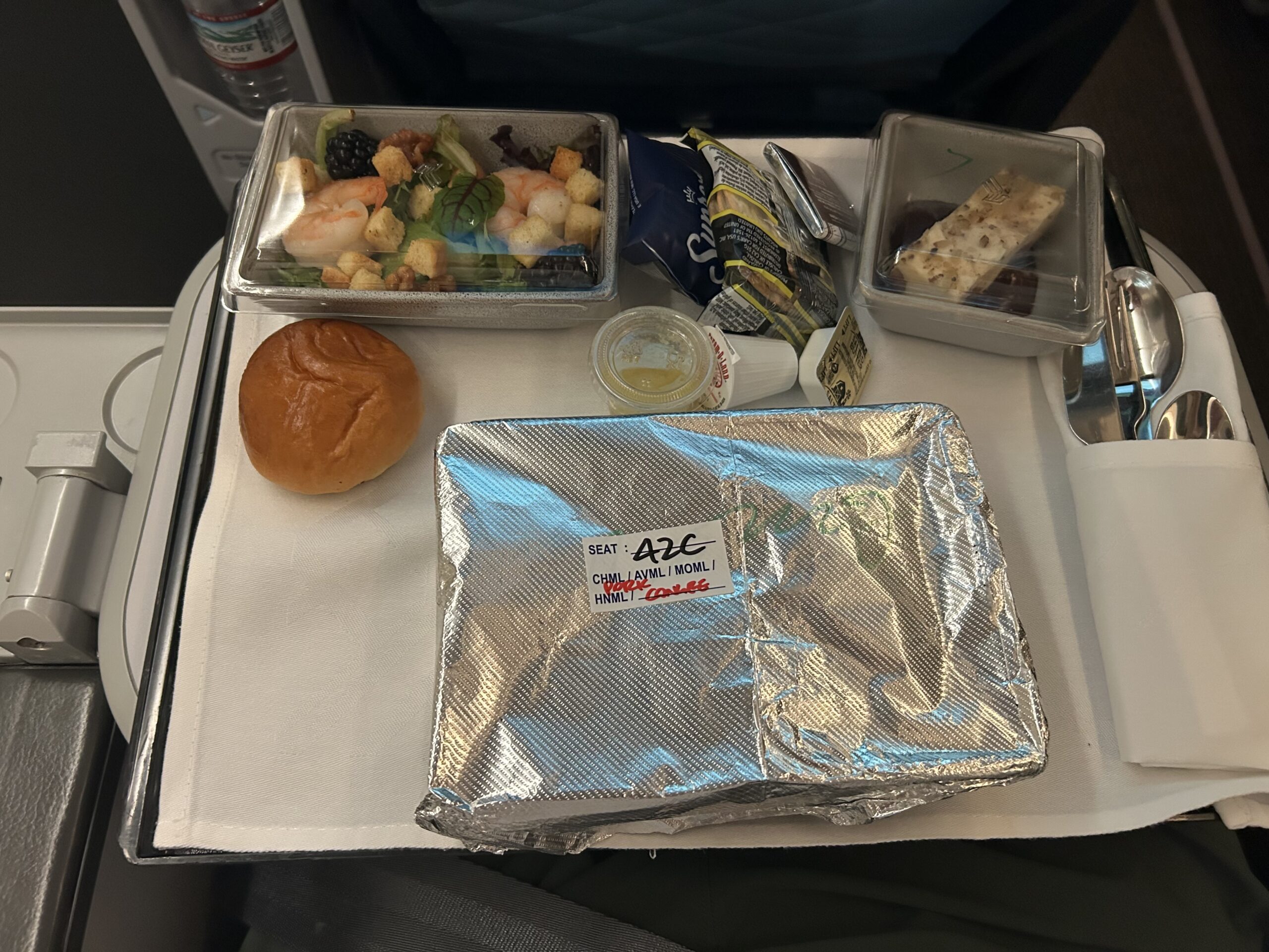 dinner roll, salad, and a foil-wrapped meal on an airline tray