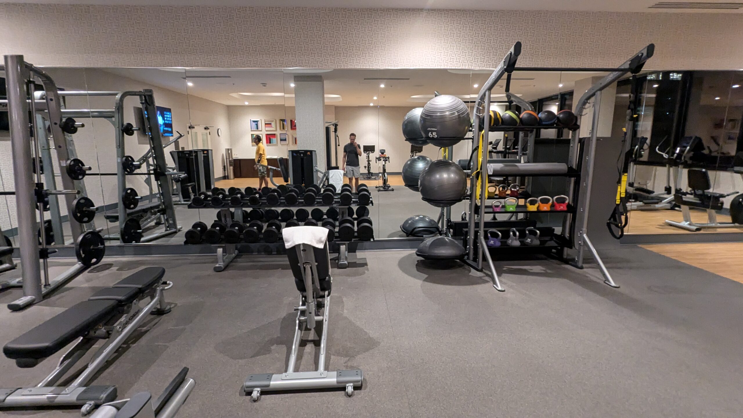 Hotel gym with benches, free weights, squat rack, and medicine balls. 